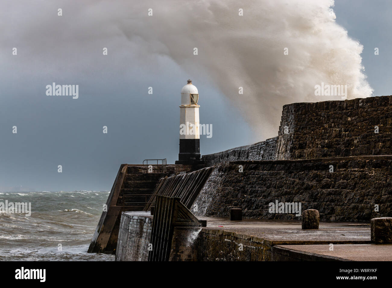 Ozean Wellen brechen über einen Hafen Wand neben einem Leuchtturm an einem stürmischen Tag (Porthcawl, Wales, Vereinigtes Königreich) Stockfoto