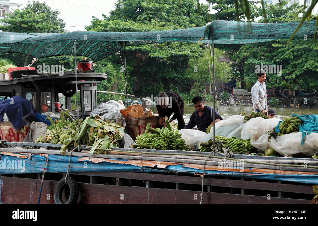 Vietnamesische Volk Transport viele Bündel Bananen bis zur Auslieferung für Saigon auf dem Wasserweg, Bootsanlegestelle am Flußufer am Tag, Ho Chi Minh City, Vietnam Stockfoto