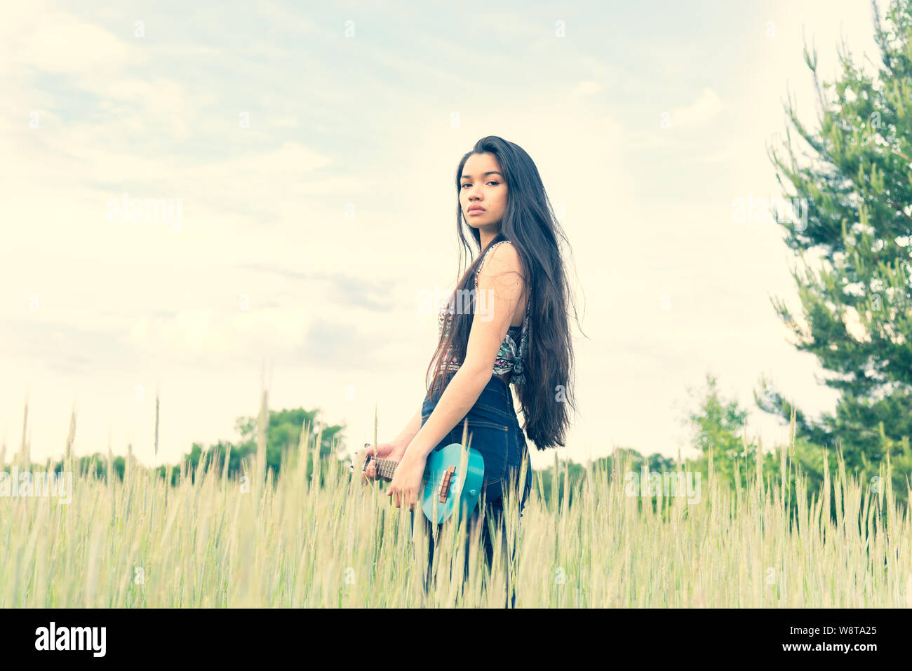 Junge schöne asiatische Frau mit sehr langen Haaren und eine Ukulele im Freien Stockfoto