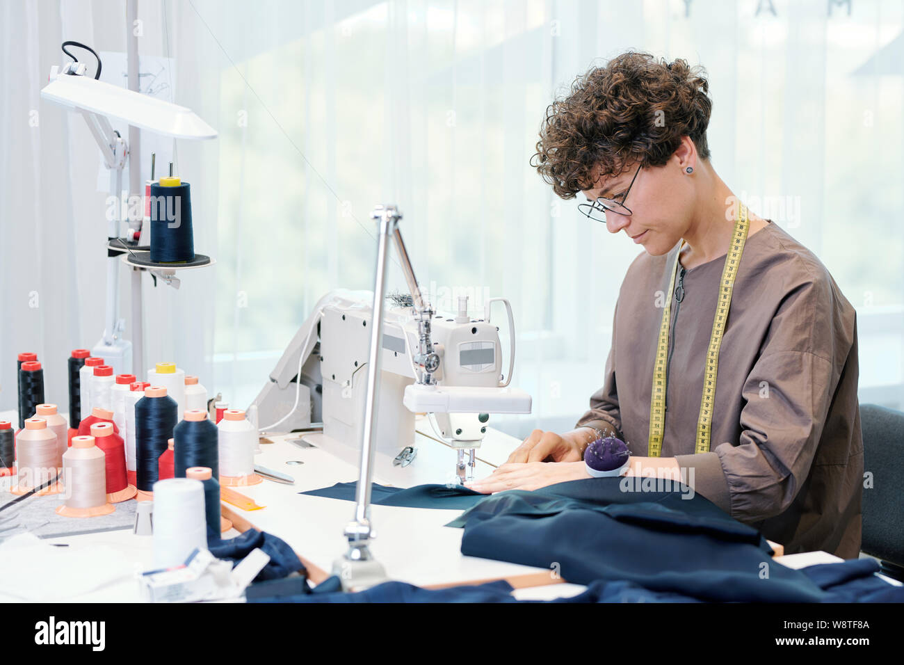 Hübsche junge Näherin sitzt von Nähmaschine und Verarbeitung blau Textil Stockfoto