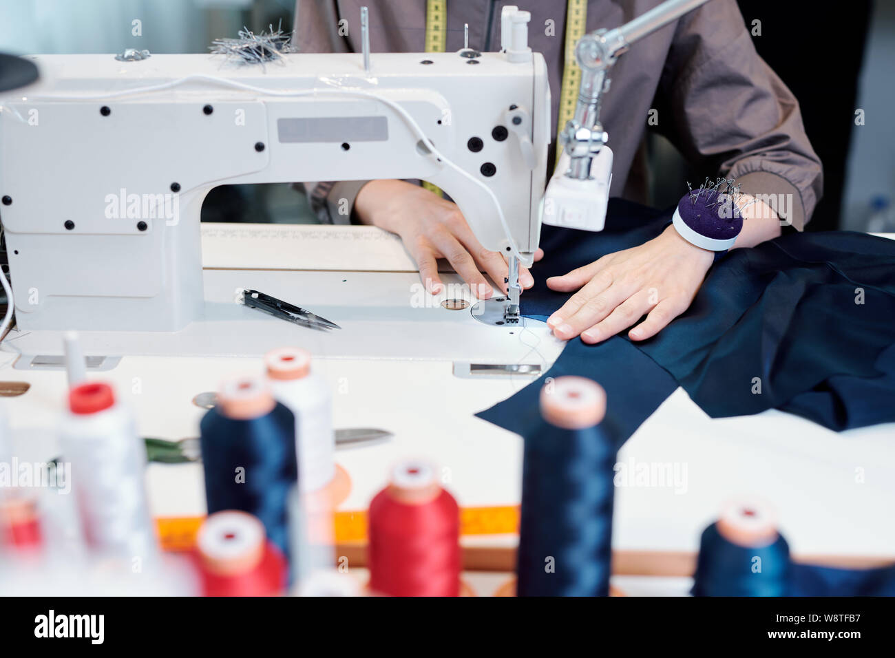 Weibliche Hände maßgeschneiderte bewegenden Stück blau Textil während des Nähens von Maschine Stockfoto