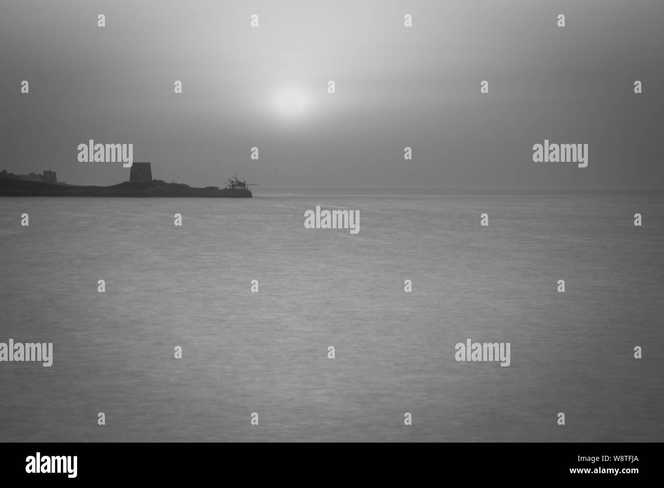 Sonnenuntergang im Sommer vor der Küste der Halbinsel Gargano, auf dem Festland ist ein alter Wehrturm und ein Haus namens Trabucchi, Italien Stockfoto