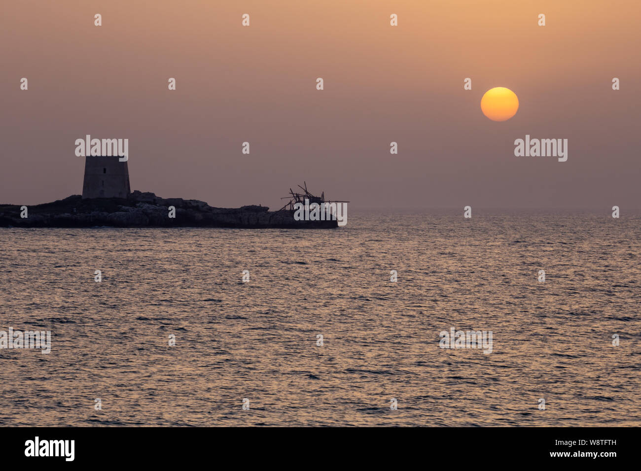 Sonnenuntergang im Sommer vor der Küste der Halbinsel Gargano, auf dem Festland ist ein alter Wehrturm und ein Haus namens Trabucchi, Italien Stockfoto