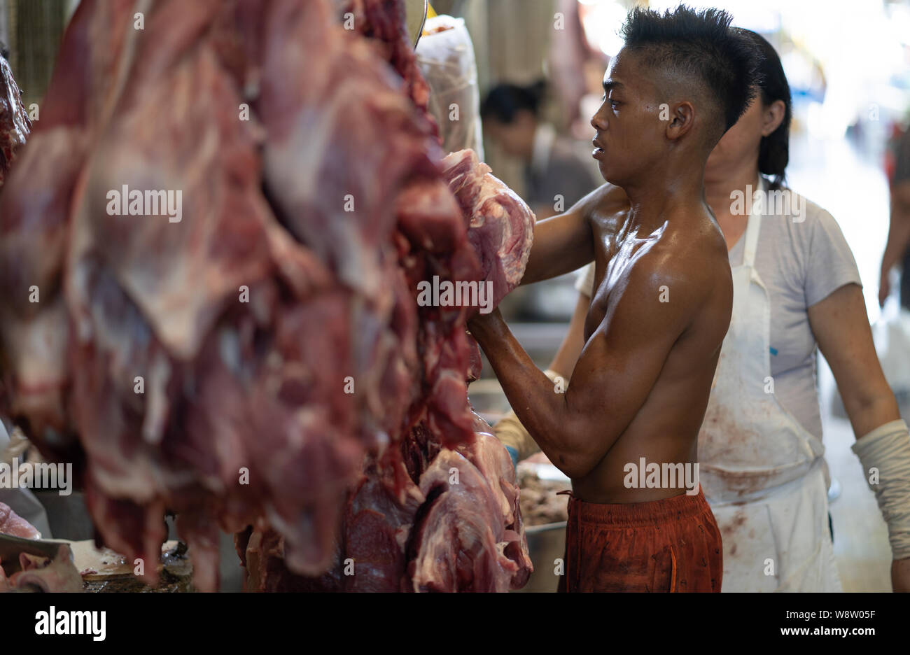 Ein Junge Griffe hängenden Schlachtkörper von Fleisch innerhalb der CO2-Markt, Cebu City, Philippinen Stockfoto