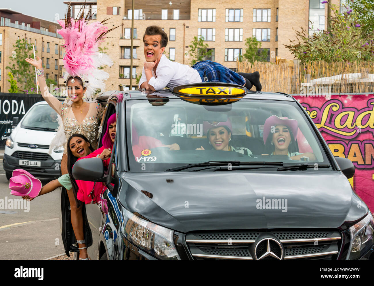 Lady Boys of Bangkok, Edinburgh Festival Fringe, Schottland, Großbritannien als Drag Artists und Zwerg in farbenfrohen Kostümen und Kopfschmuck ins Taxi kramen Stockfoto