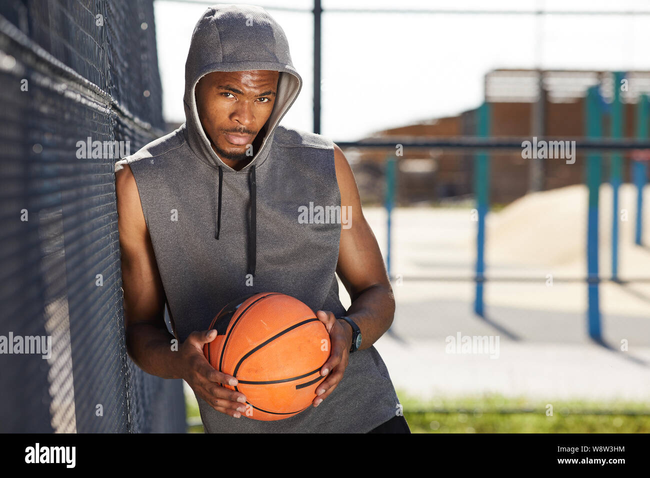Taille bis Porträt des zeitgenössischen afroamerikanischen Mann mit Basketball Ball mit Kamera schaut während der Sportplatz im Freien Raum darstellen, kopieren Stockfoto