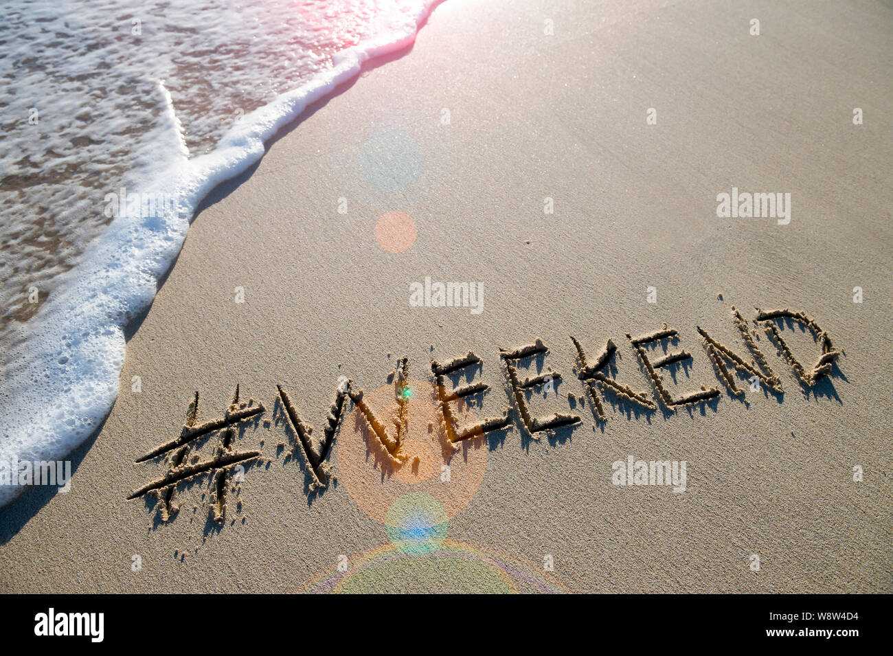 Modernes reisen Nachricht für den Strand mit einem Social Media - freundliche Hashtag mit dem Wort 'Wochenende' in sanften Sand mit ankommenden Welle geschrieben Stockfoto