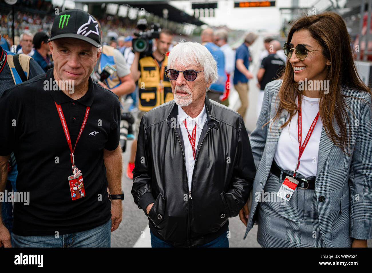 Randy Mamola (L), der ehemalige amerikanische Grand Prix Motorrad Racer, Bernie Ecclestone (C), Ehrenvorsitzender der Formel 1 Gruppe mit seiner Frau, Fabiana Flosi Spaziergang durch die startaufstellung vor der Österreichischen MotoGP Grand Prix Rennen. Stockfoto