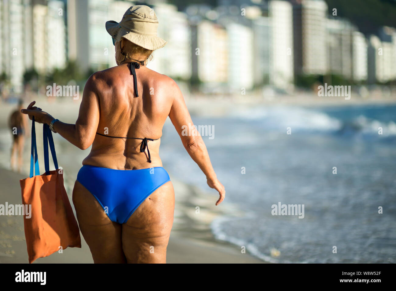 Nicht erkennbare Frau in Blau Badeanzug und Sonnenhut Wandern am Ufer des Copacabana Beach in Rio de Janeiro, Brasilien Stockfoto