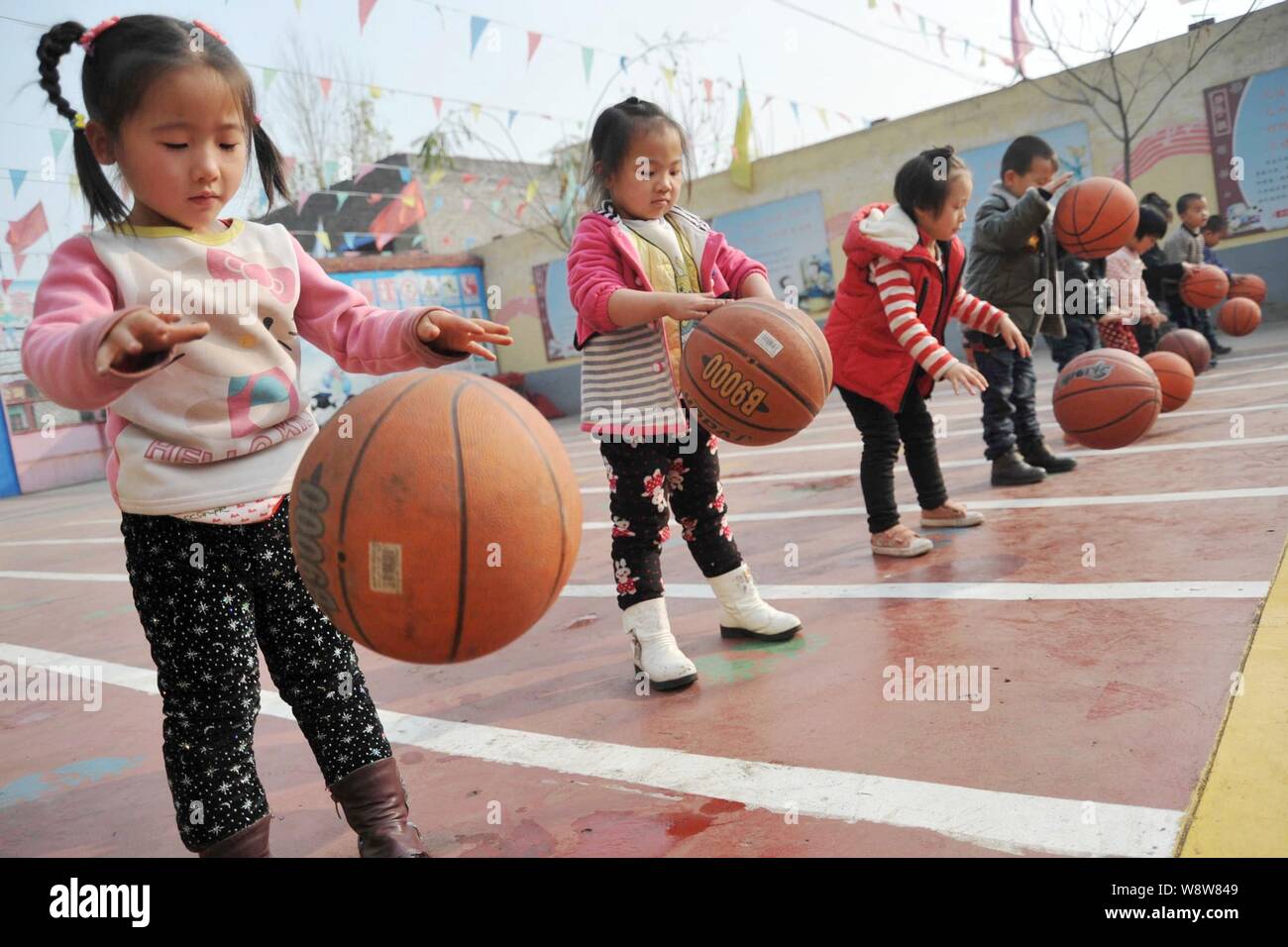 Junge chinesische Kinder hinter sich gelassen von ihren Wanderarbeitnehmer Eltern spielen mit basketbälle auf dem Spielplatz zu einem ländlichen Kindergarten in Xinjiang, Grafschaft, Stockfoto