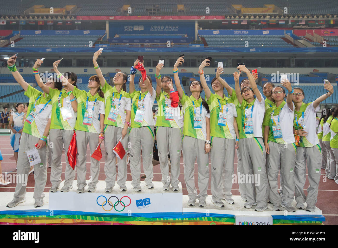 Freiwillige verwenden ihre Smartphones selfies auf einem Podium während einer Abschiedsfeier im Nanjing Olympic Sports Center Stadion während der 2014 Summ Stockfoto