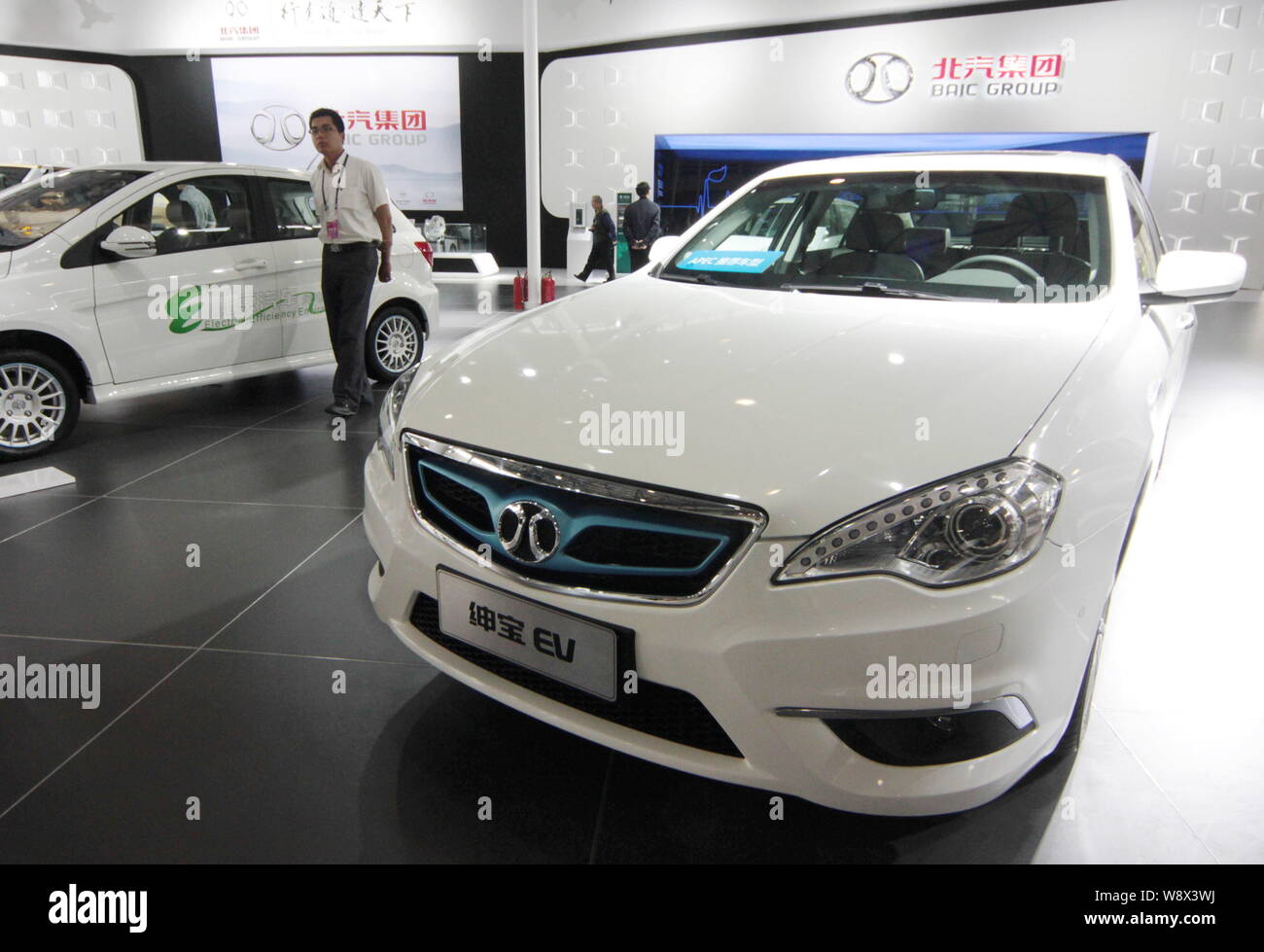 ---- Ein chinesischer Mitarbeiter Spaziergänge hinter einem shenbao Elektrofahrzeug von baic (Beijing Automotive Industry Holding Co.) Gruppe während einer Ausstellung in Beiji Stockfoto