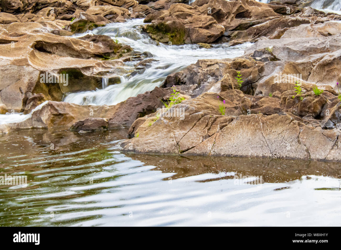 Wasser stürzt nach einigen Felsen in einen flachen Teil eines Flusses, zwischen Dämme. Stockfoto