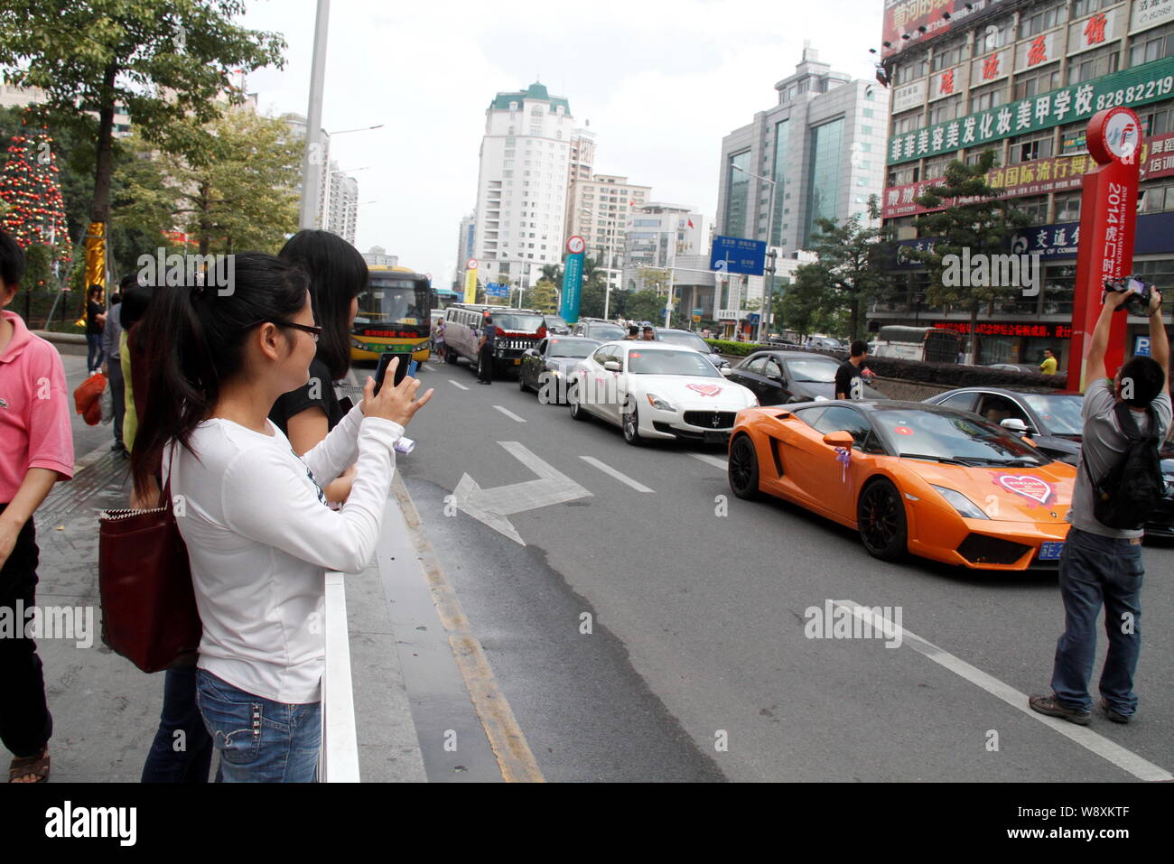 Fußgänger nehmen Sie Fotos oder Blick auf Sport, Autos und andere Fahrzeuge, die in der Hochzeit Parade auf der Straße während des Chinesischen Unternehmer Chen Junliang's weddin Stockfoto