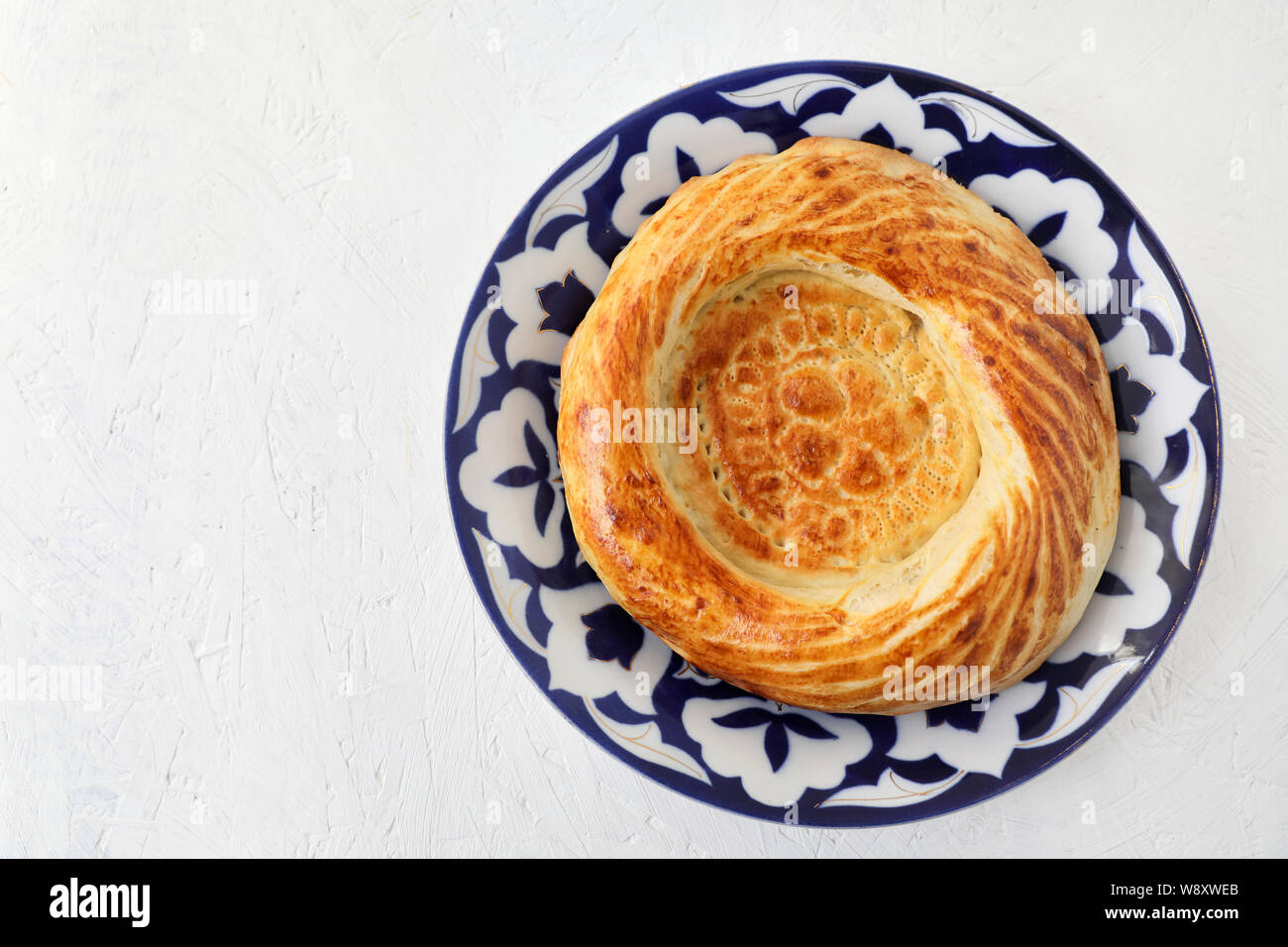 Die traditionellen Zentralasiatischen Brot, tandoor Pellet. Auf einem nationalen Stil Teller. Weiße strukturierte Hintergrund. kopieren. Stockfoto