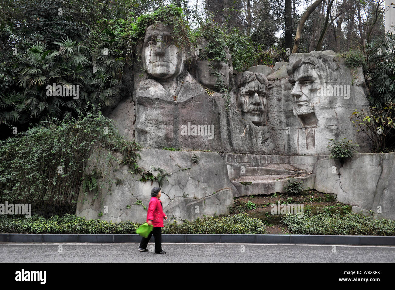 Eine chinesische Frau geht vorbei an der Steinmetzarbeiten des US-Präsidenten von China Nachbau des Mount Rushmore National Memorial bedeckt mit Vegetation ein Stockfoto