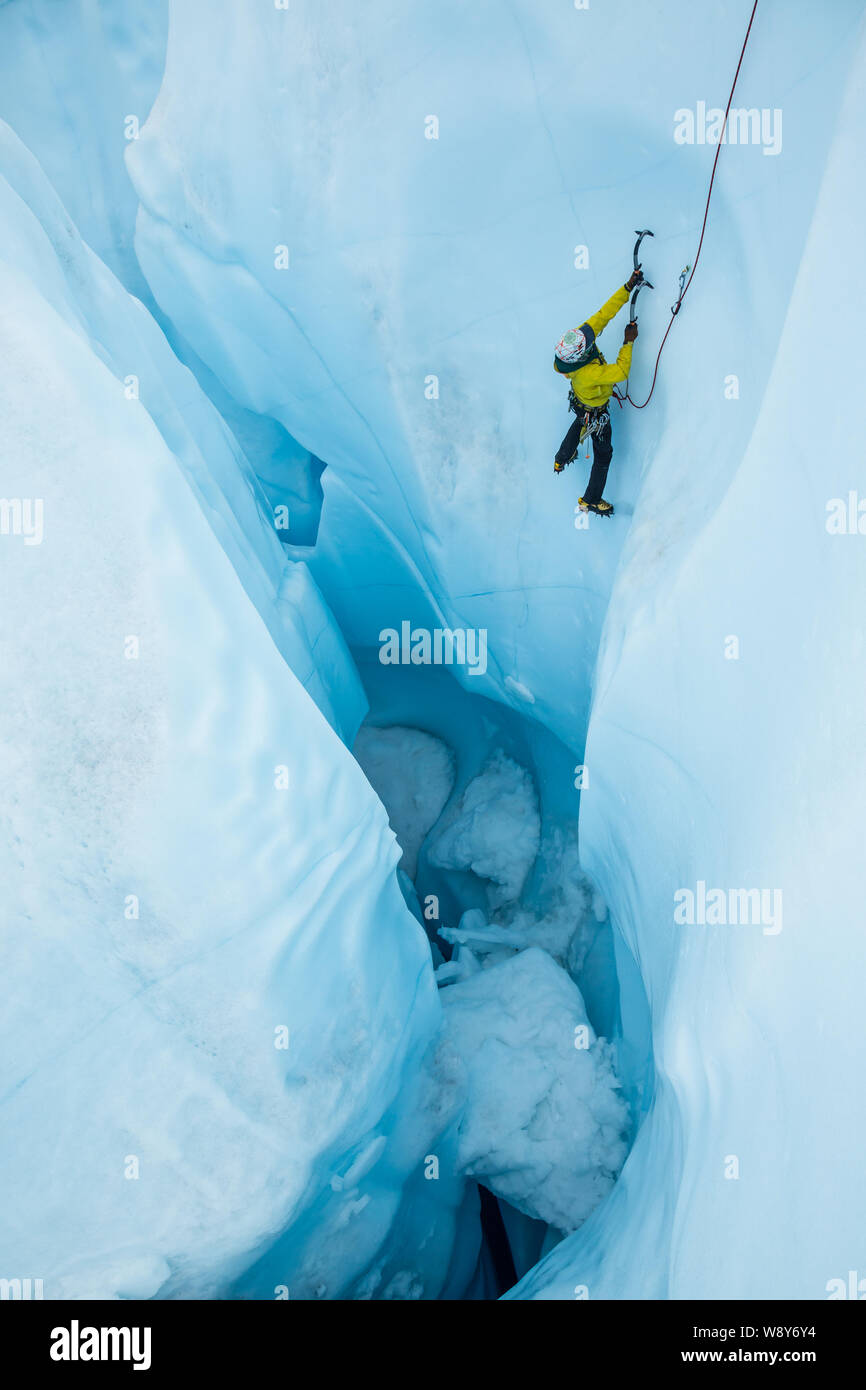 Mann nach dem Führer einer steilen Eis Aufstieg aus einem überhängenden Wand eines Moulin auf der Matanuska Gletscher in Alaska. Stockfoto