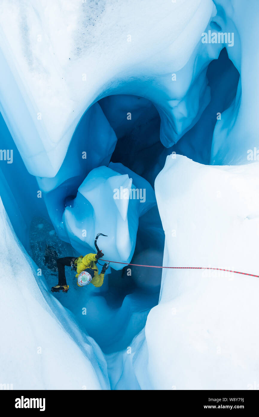 Ice climber Aufsteigend aus einem Moulin auf einem Gletscher. Im Inneren des Moulin ist eine große Säule aus Eis ist er mit bis zu klettern und heraus. Stockfoto