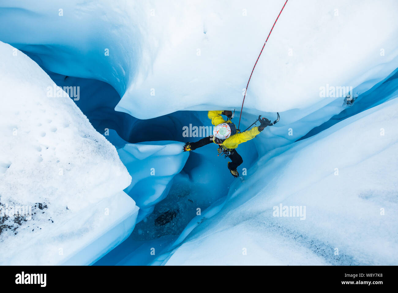 Ice climber, die einen Fuß in eine vertikale Säule aus Eis frei stehend in einem massiven moulin Tunnel auf der Matanuska Gletscher. Stockfoto