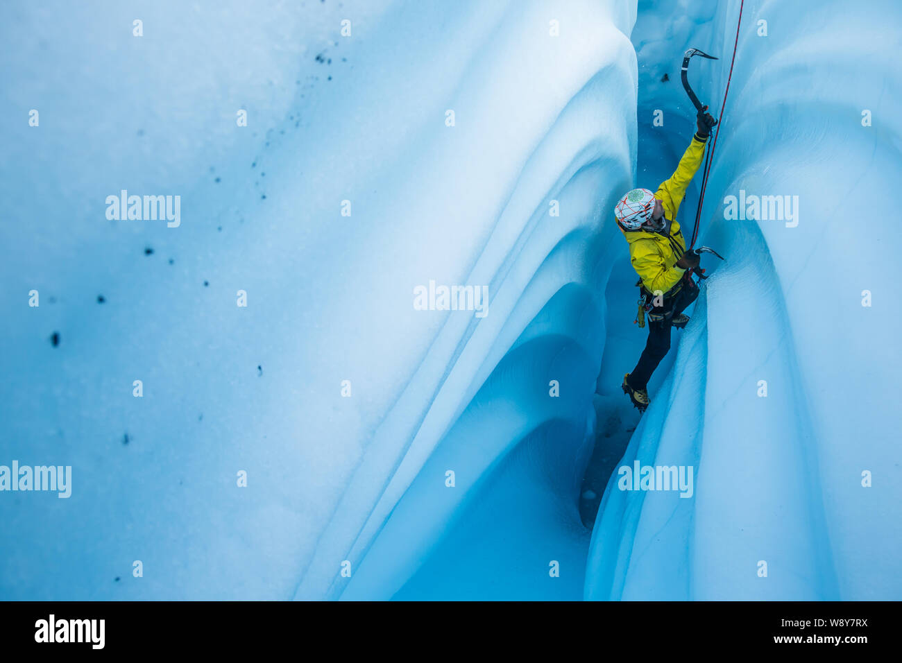 Ice climber aufsteigend eine schmale Passage in einem Gletscher eis Höhle mit Wellenlinien von schmelzendem Eis schneiden in den Wänden. Stockfoto