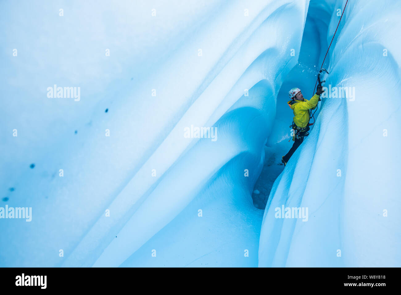 Eisklettern eine Eishöhle auf der Matanuska Gletscher, ein Mann schlägt Eis Chips, wie er sein Werkzeug in die Mauer schwenkt nach oben zu klettern. Stockfoto