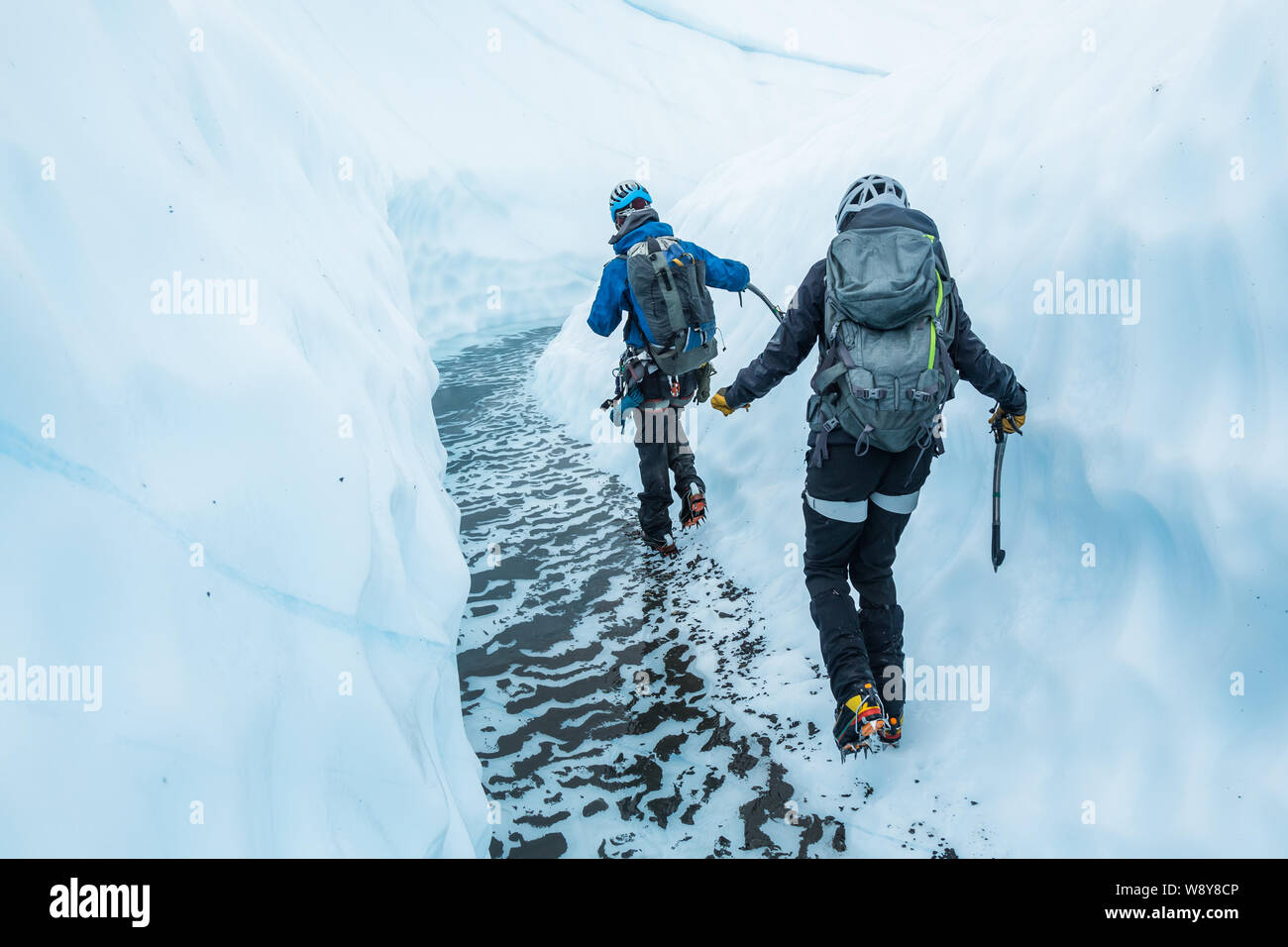 Junger Mann und Frau sorgfältig treten durch einen schmalen Canyon Schnitt von Gletschereis. Die perfekt klare Wasser unter Ihnen ist tief und kalt. Stockfoto