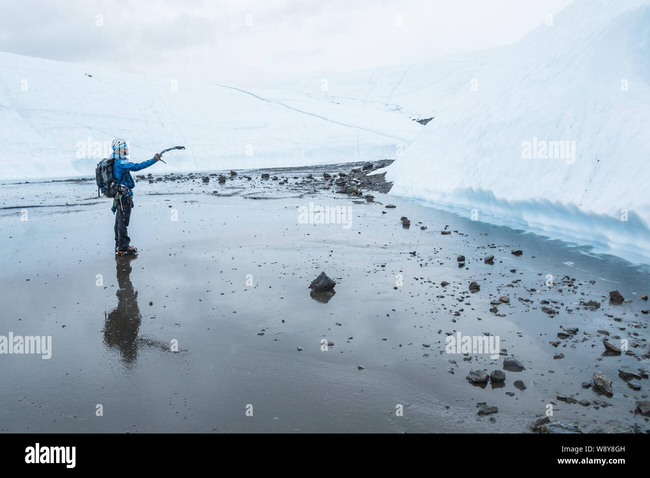 Ice climber zeigt seine Axt an der Eiswand vor ihm, eine Linie im Regen in Alaska zu klettern. Stockfoto