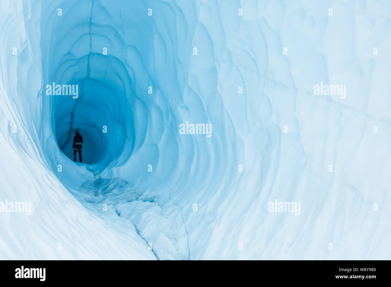 Eine junge Frau wandert in die Tiefen einer riesigen eishöhle in einem Gletscher in Alaska. Stockfoto