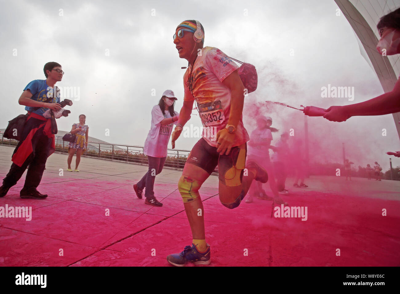 Ein Teilnehmer wird durch einen Mitarbeiter mit farbigem Pulver gesprüht, als er durch eine Farbe Station läuft während der fünf Kilometer langen Colour run Ereignis in Shangha Stockfoto