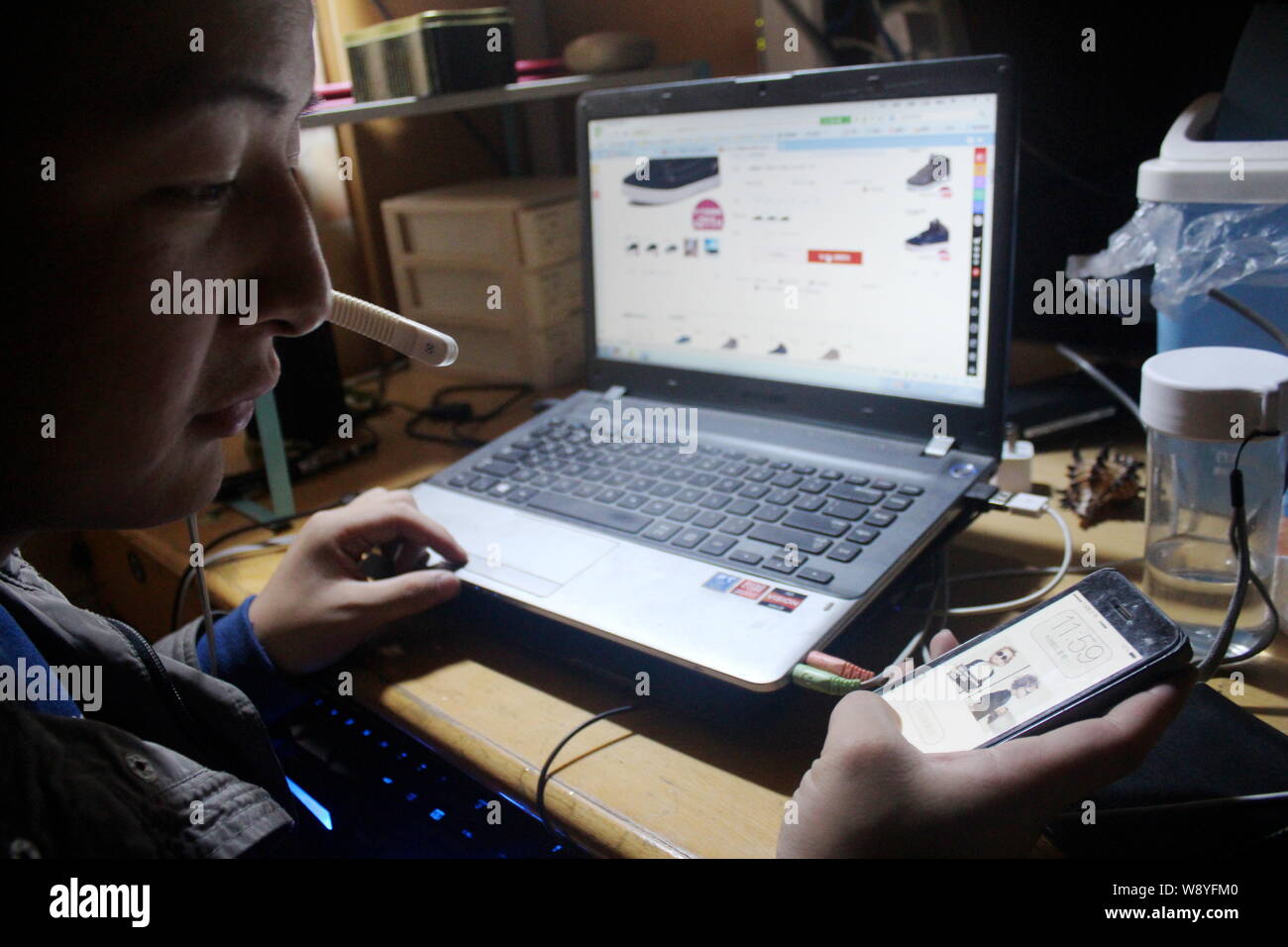 Ein chinesischer Student sucht online Shops auf seinem Laptop Computer und Smartphone für den 11. November Singles Tag Einkaufsbummel vorbereiten, bevor midnigh Stockfoto
