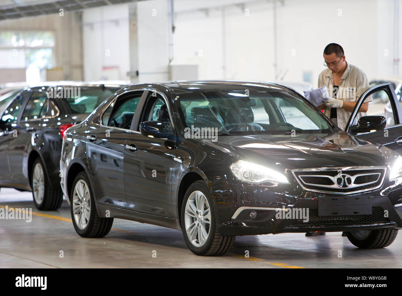 ---- Ein chinesischer Arbeiter prüft BAIC E 150 Elektrofahrzeugen an eine automatische Anlage von baic (Beijing Automotive Industry Holding Co.) Gruppe in Peking, China Stockfoto
