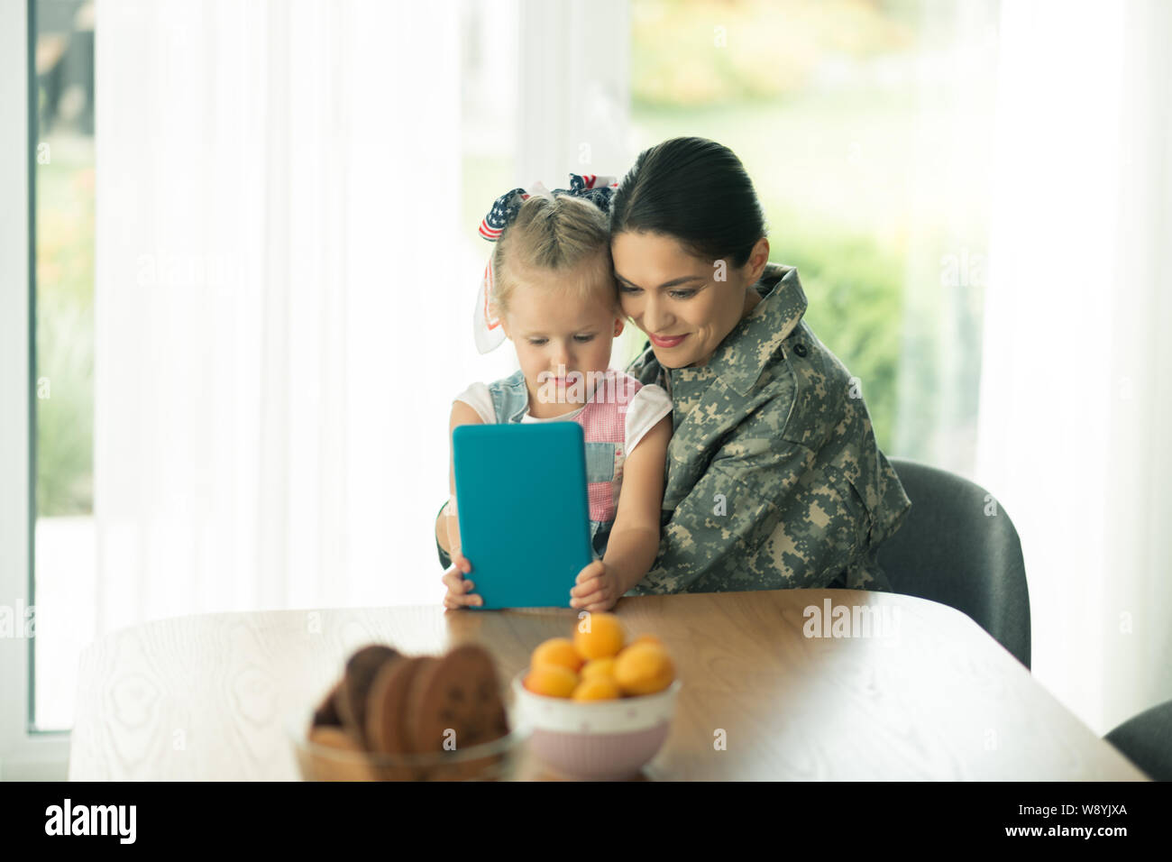 Tochter sitzen in der Nähe von Mama in Uniform und Cartoon beobachten Stockfoto