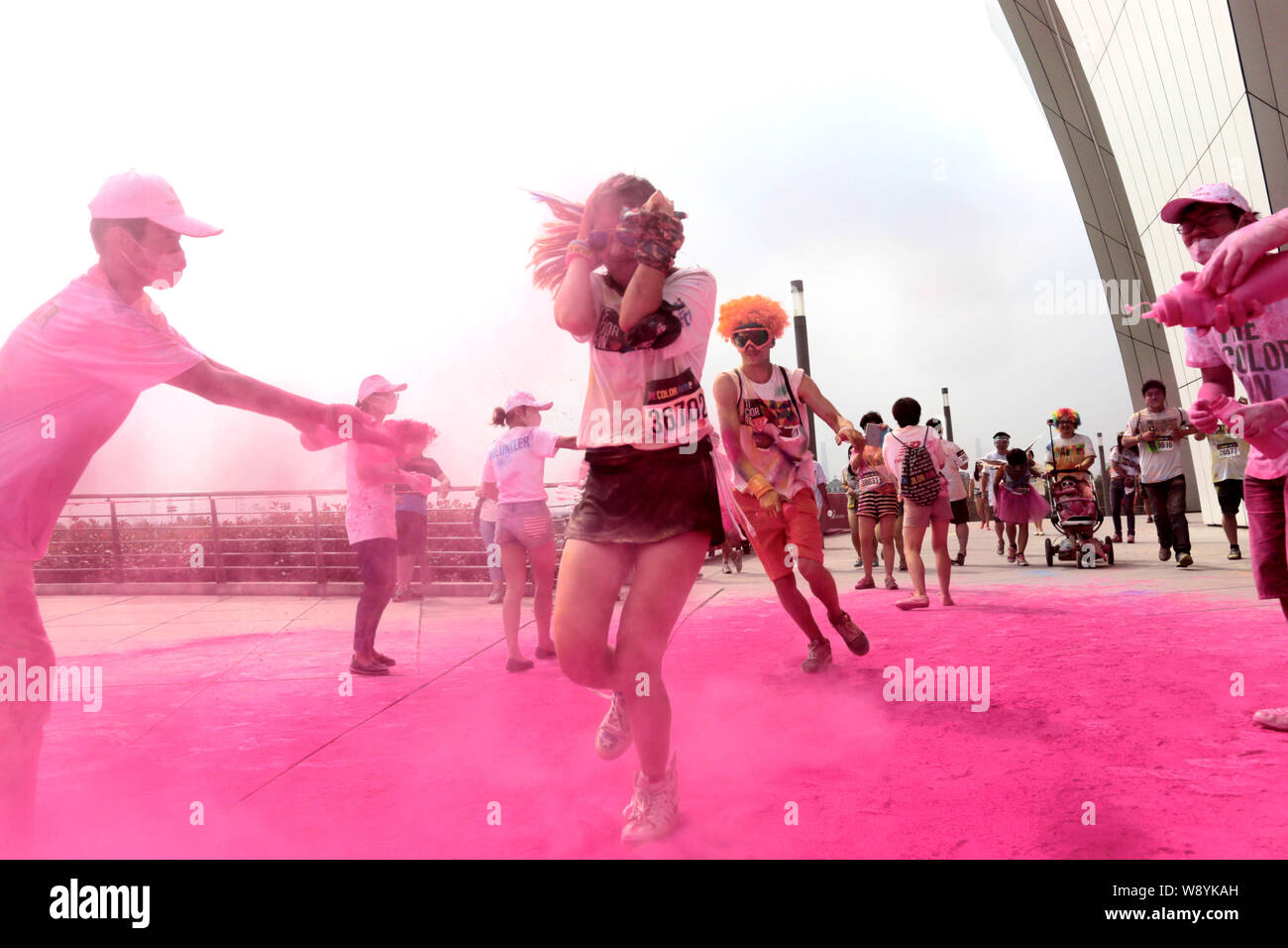 Die Teilnehmer werden durch Mitarbeiter mit farbigem Pulver gesprüht, wie Sie durch eine Farbe Station während der fünf Kilometer langen Colour run Ereignis in Shangha ausführen Stockfoto