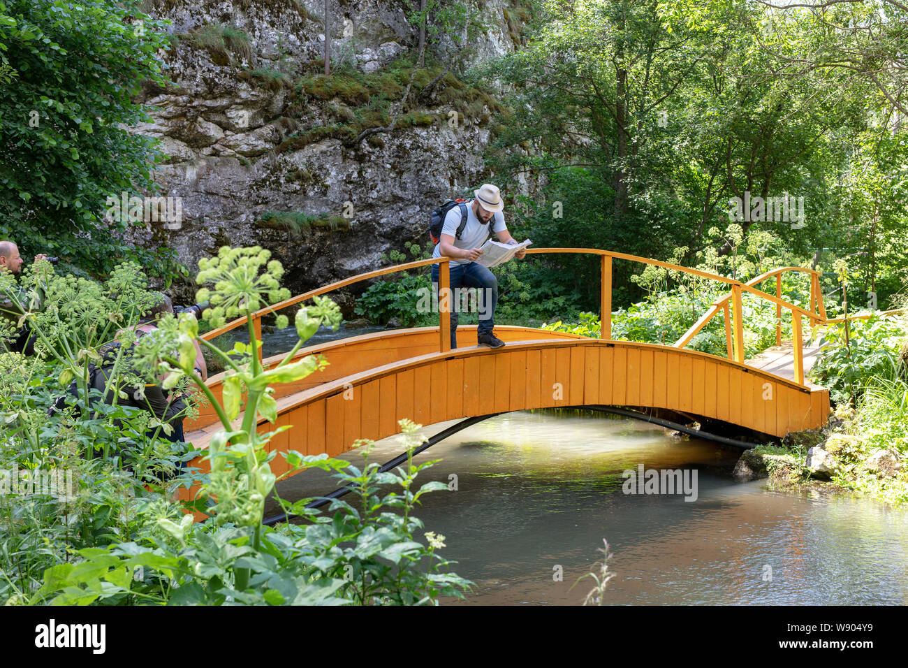 Ein Mann mit einem Rucksack studiert eine Karte im Freien stehend auf einer Brücke. Konzept des Ökotourismus, unabhängige Reisen. Fotografen Bilder von ihm Stockfoto