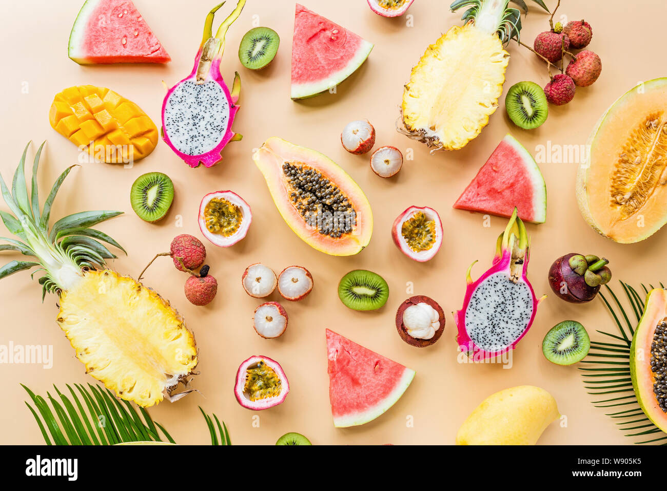 Frische exotische Früchte und tropischen Palmen Blätter auf pastellorange Hintergrund - Papaya, Mango, Ananas, Passionsfrucht, Dragon Obst, Trauben, lichee, Kiwi Stockfoto