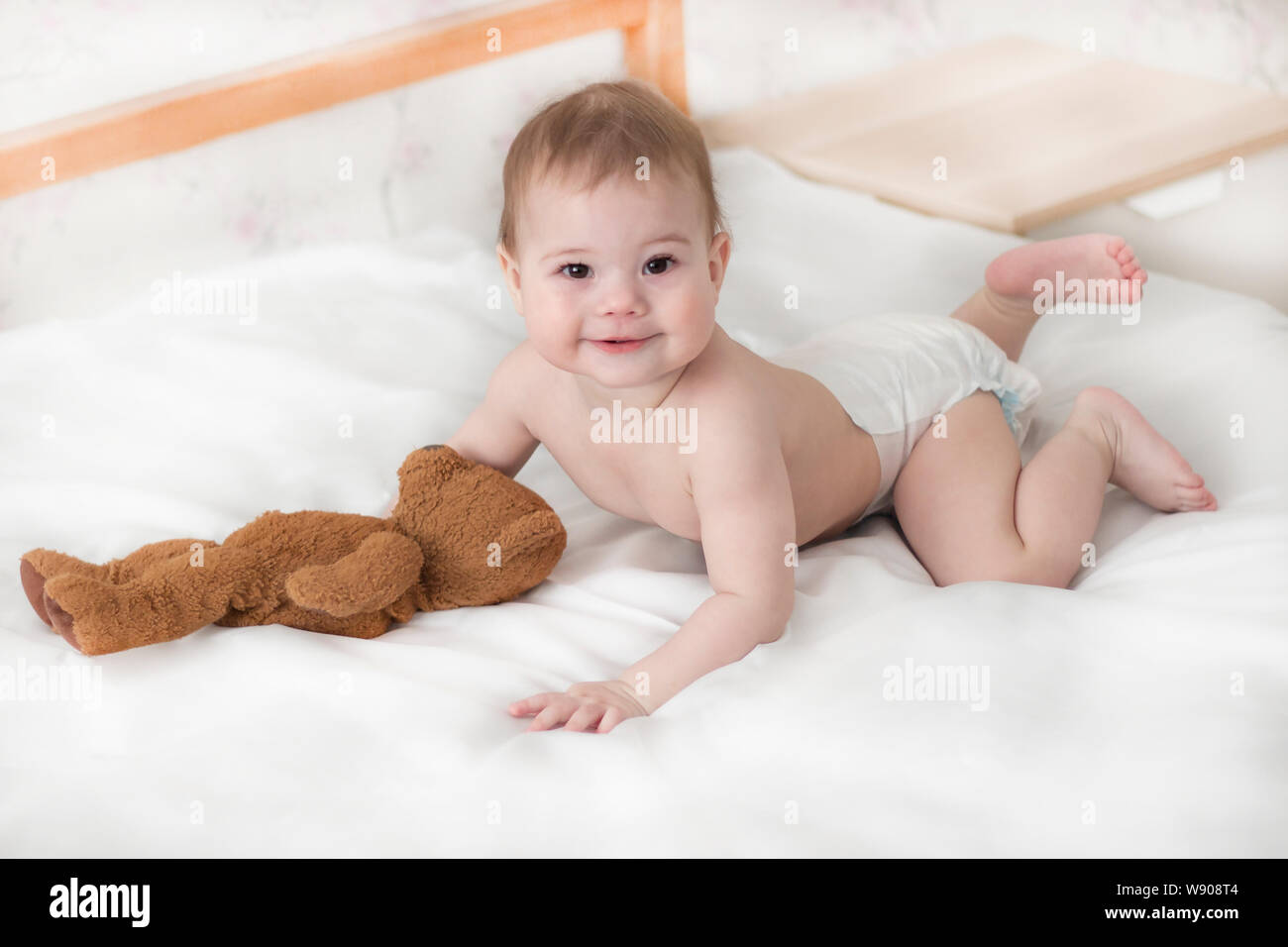 Fröhliches baby junge Mädchen in eine Windel liegen mit einem Teddybären. Cute Baby in eine Windel krabbeln auf dem Bett, schauen in die Kamera Baby mit einem Spielzeug tragen Stockfoto