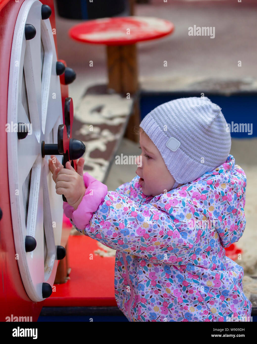 Kleines Mädchen auf dem Spielplatz. Ein Jahr alten Kind in einen Hut und Mantel spielt mit der Kinder Karussells und Sportgeräte. Ein Kind geht i Stockfoto