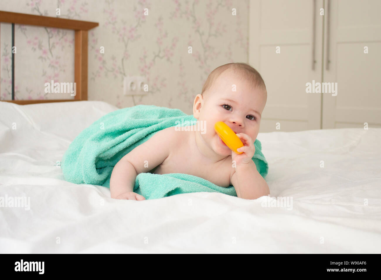 Baby Kaukasier Mädchen Jungen 5 Monate in ein Handtuch gewickelt, knabbert an einem Bagel, Soft Focus Stockfoto