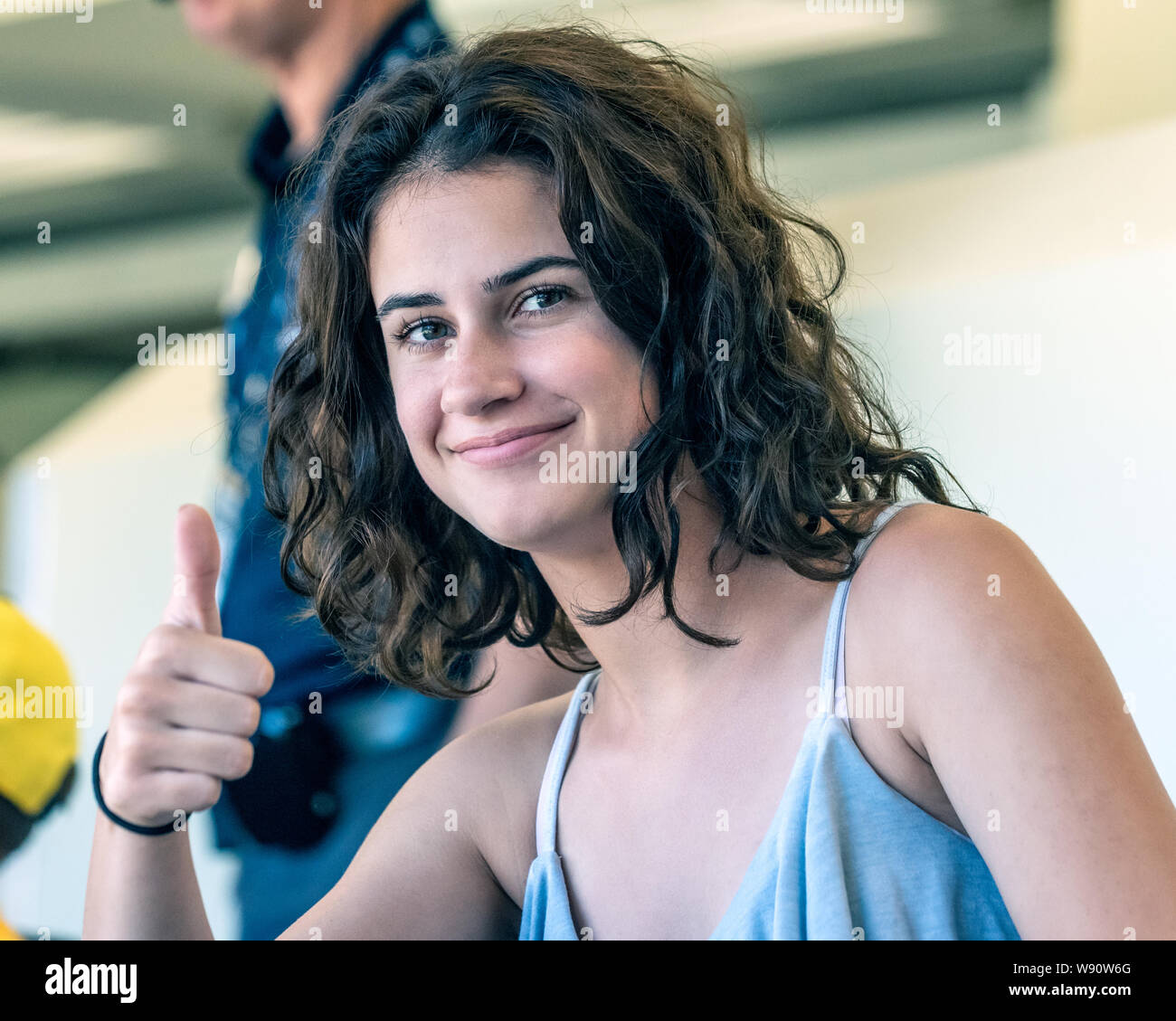 Hübsche Teenager weiblichen Fan mit positivem Daumen oben unterzeichnen und Lächeln, während im Stadion sitzt. Stockfoto