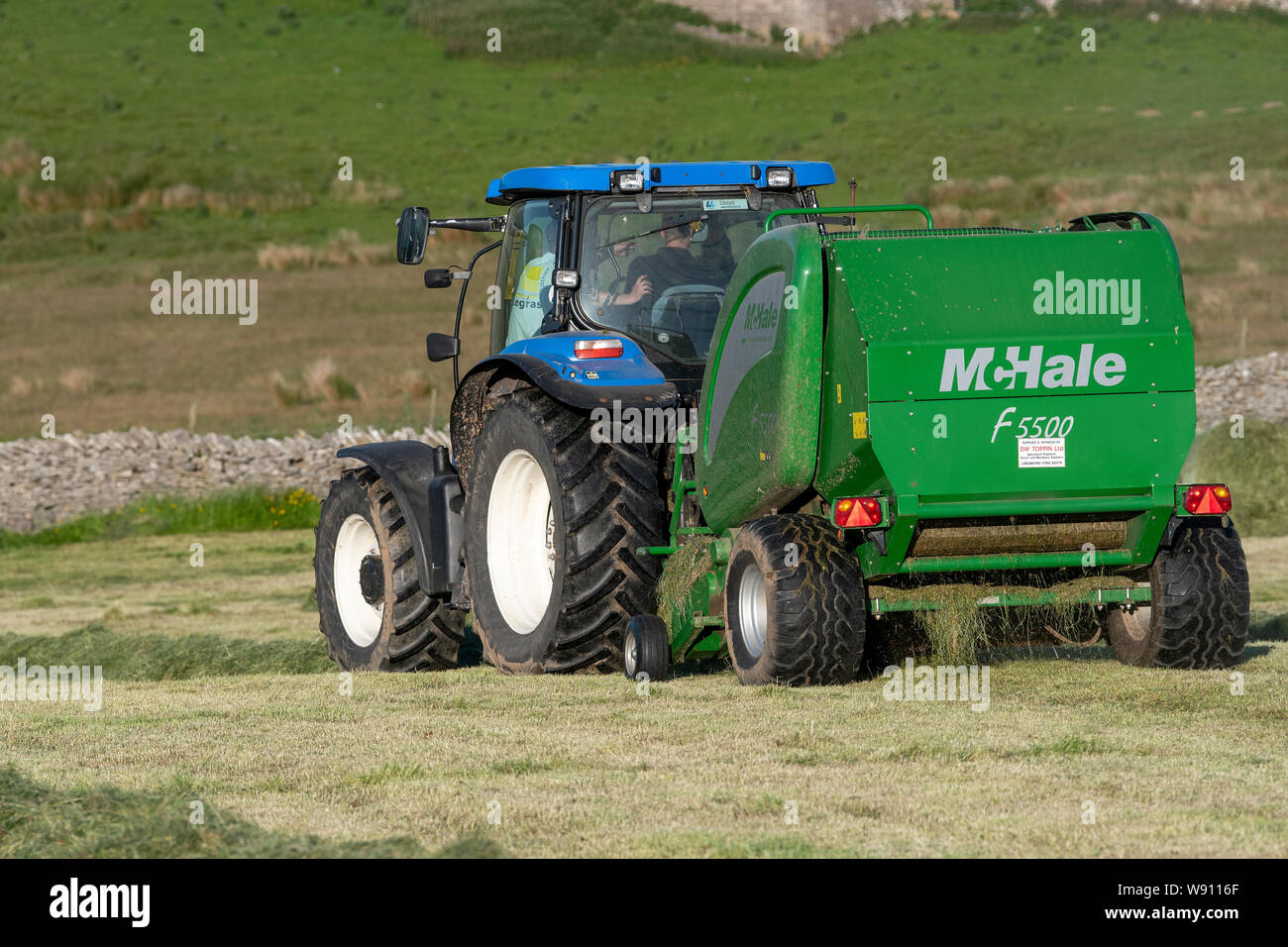 Die heulage Erntegut auf der Alm mit einem New Holland T6030 und ein McHale 5500 Ballenpresse. Cumbria, Großbritannien. Stockfoto