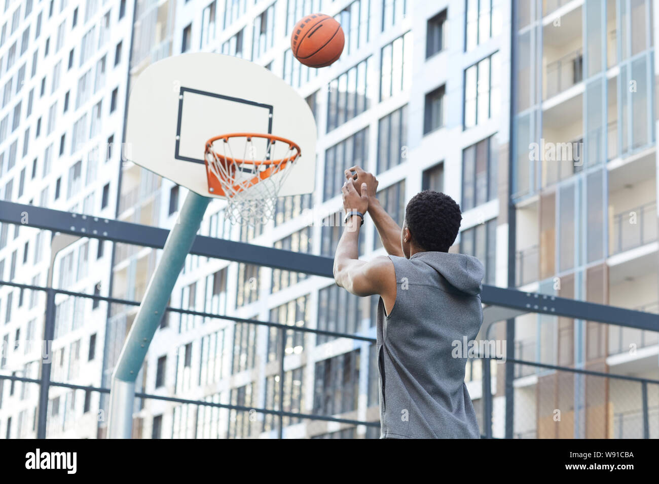 Rückansicht des afrikanischen Mann schießen Slam Dunk in Baskettballplatz draußen im städtischen Raum einstellen, kopieren Stockfoto