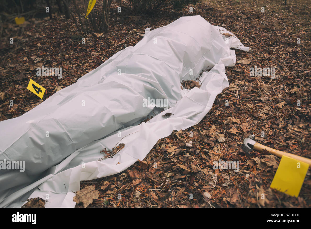 Opfer eines Gewaltverbrechens unter einem Blatt in einem ländlichen Hof. Mit Beweis Marker und mordwaffe. Stockfoto