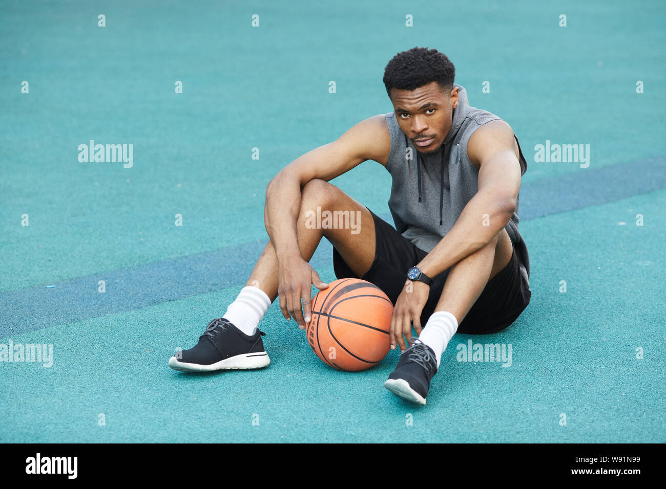 Volle Länge Portrait von Stattlichen afrikanische Sportler sitzen auf dem Boden im Basketball Court und Kamera, kopieren Raum Stockfoto
