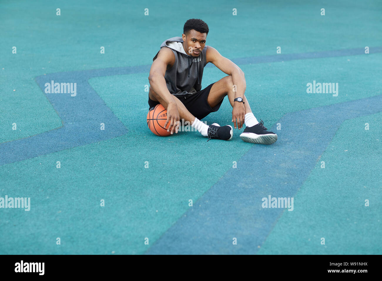 Weitwinkel Portrait von Stattlichen afrikanische Sportler sitzen auf dem Boden im Basketball Court und Kamera, kopieren Raum Stockfoto
