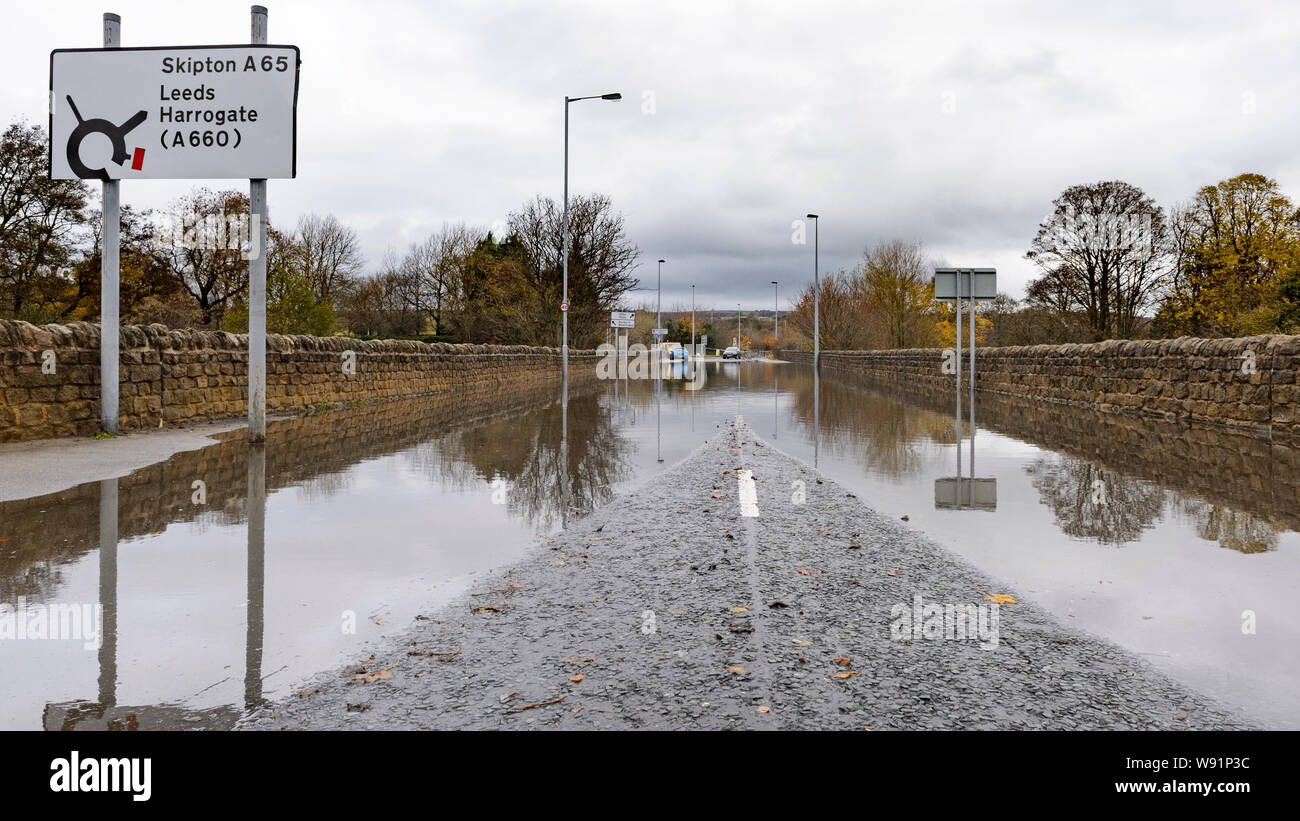 Überschwemmung - Überflutete Straße (autofrei) mit Bäumen & Zeichen in ständigen Hochwasser - Burley in Bösingen, Yorkshire, England, UK wider. Stockfoto