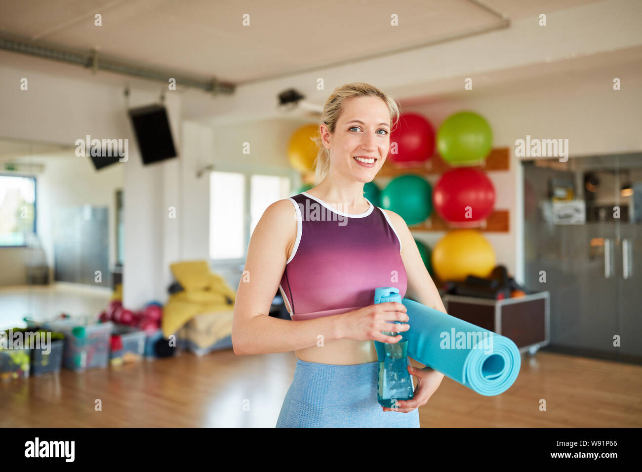 Junge Frau als Trainer mit Yoga Matte und Wasserflasche in der Turnhalle Stockfoto