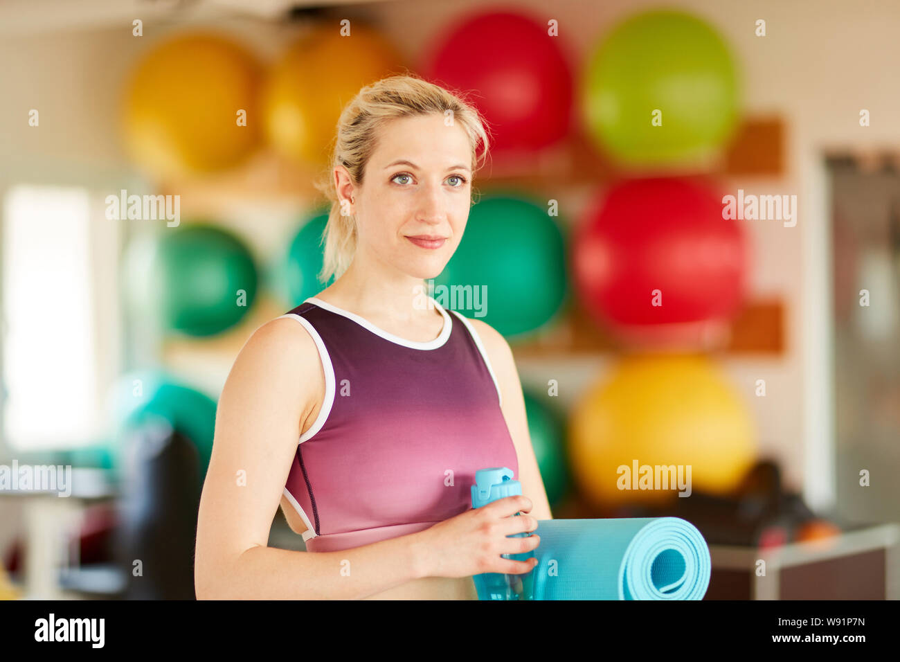 Sportliche Frau in der Turnhalle als Trainer mit Yoga Matte und Wasserflasche Stockfoto