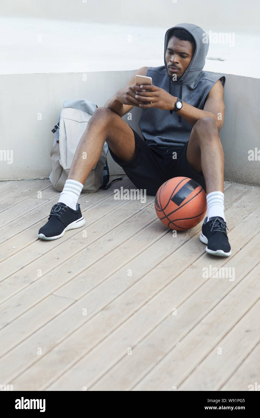 In voller Länge Porträt des zeitgenössischen afroamerikanischen Mann mit Smartphone und entspannen Sie im hoteleigenen Park, Kopie Raum Stockfoto