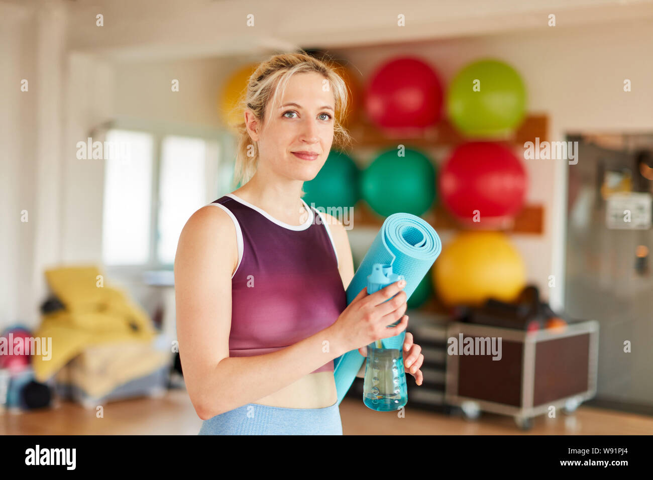 Junge Frau als Fitness Trainer im Fitnessbereich mit Yoga Matte und Wasserflasche Stockfoto