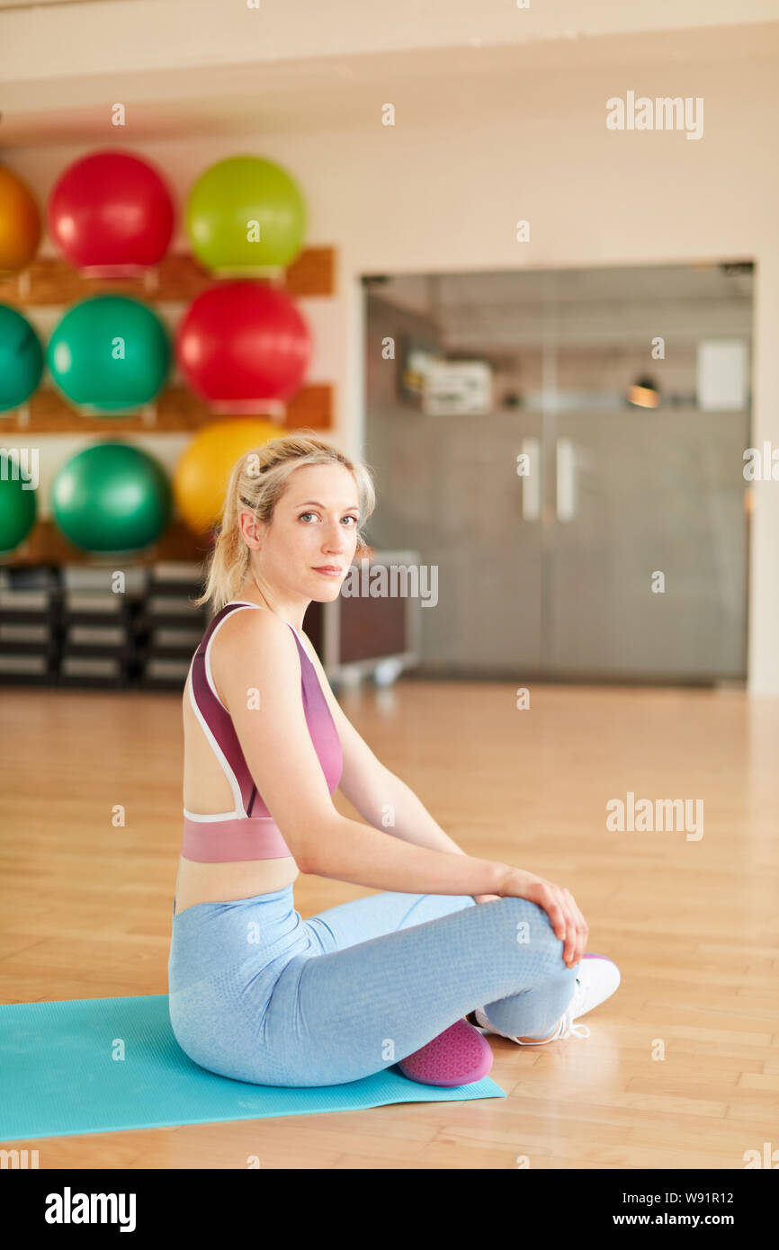 Junge Frau im Fitnesscenter sitzt entspannt auf einer Matte in einer Pause Stockfoto